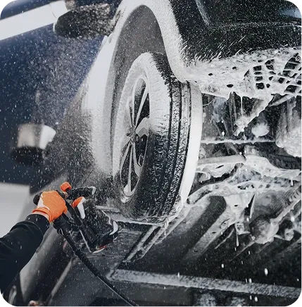 Roue de voiture recouverte de mousse, nettoyée à la lance haute pression par un gant orange