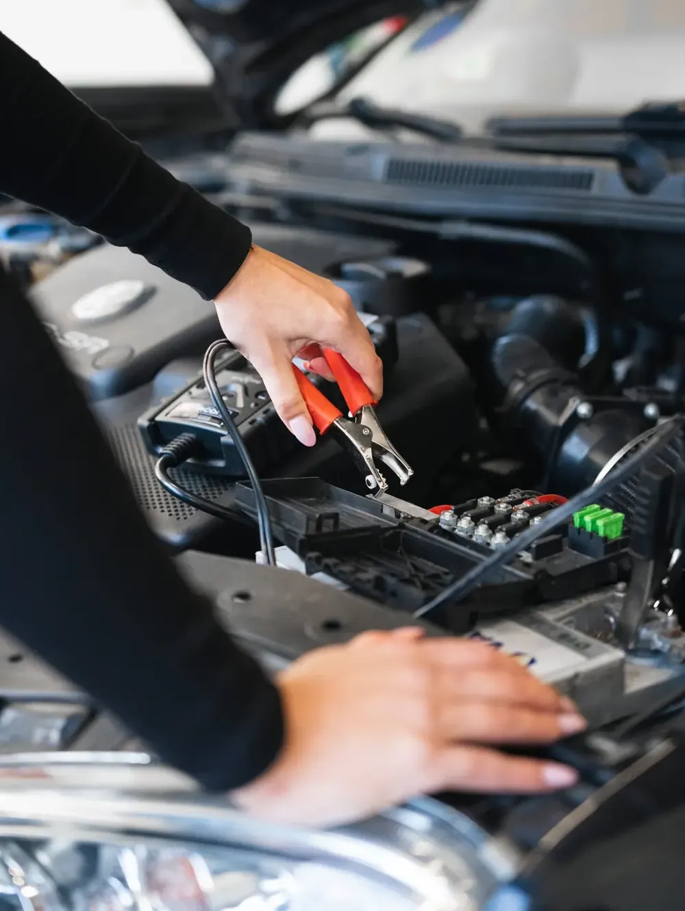 Une main saisit les pinces d’un testeur de batterie dans le compartiment moteur