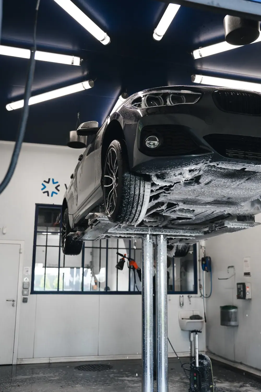 Une BMW sur un pont élévateur, recouverte de mousse, dans un box de lavage au plafond bleu