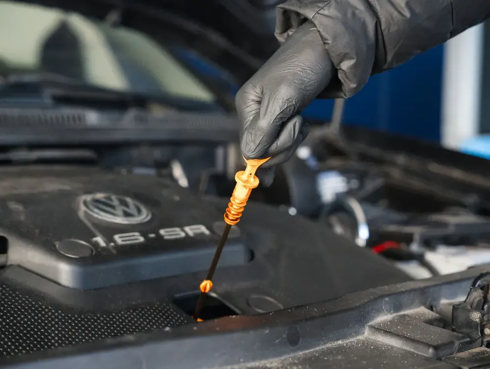 Une main gantée retire la jauge d’huile orange du moteur d’une Volkswagen