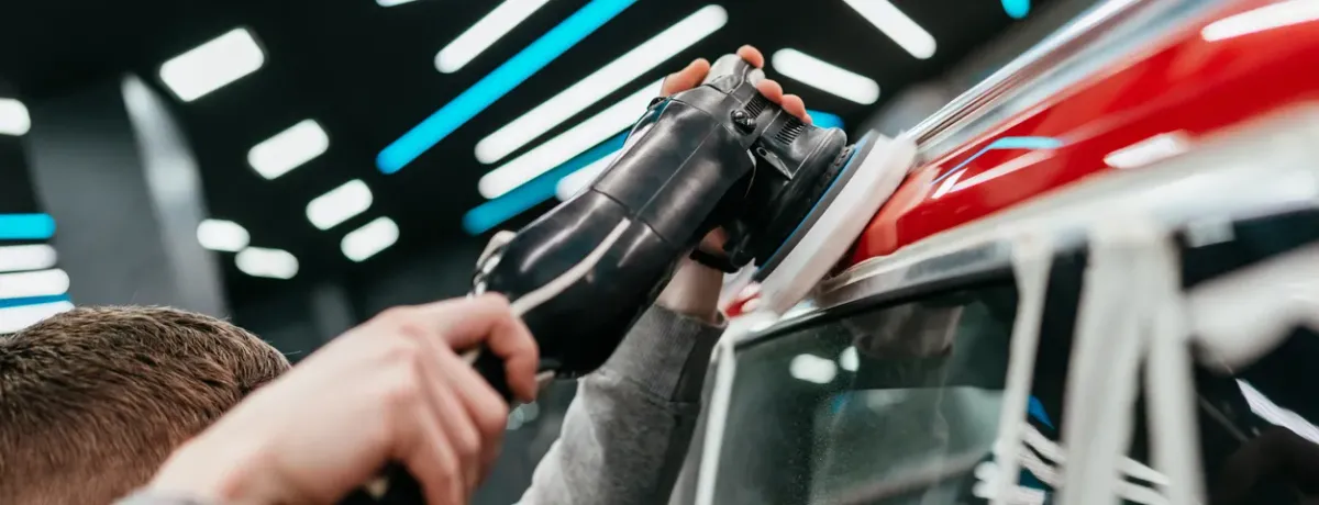Polissage de la carrosserie d'une voiture rouge à la polisseuse orbitale