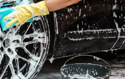 Nettoyage d'une jante de voiture noire à la main avec une éponge savonneuse