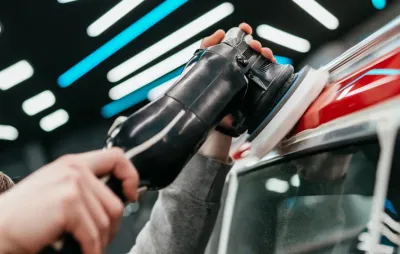 Polissage de la carrosserie d'une voiture rouge à la polisseuse orbitale