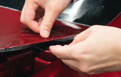 Application d'un film de protection de carrosserie (PPF) sur une voiture, mains en gros plan